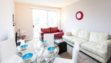 A modern living room with a glass dining table set for four, a red sofa, a white sofa, and a red wall clock.