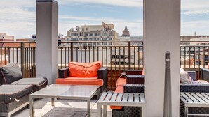 En takterrass med utemöbler, inklusive soffor och ett bord, och en utsikt över stadsbilden i bakgrunden.