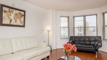 A living room with a white sofa, a black leather sofa, a floor lamp, a vase with flowers, and a framed map on the wall.