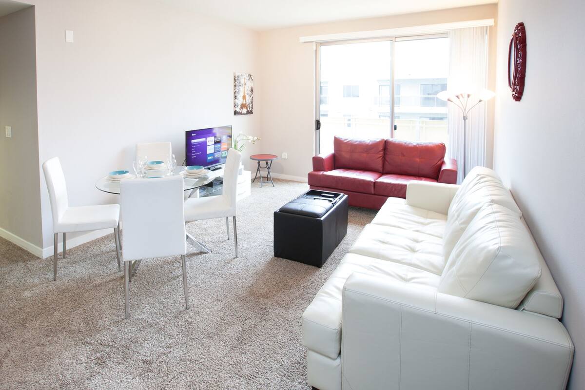 A modern living room with a white sofa, a red sofa, a dining table with chairs, and a TV.