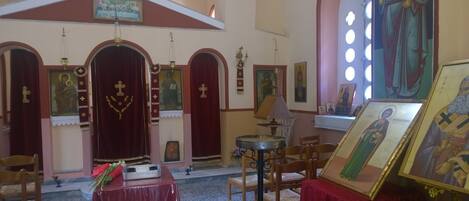 L’intérieur d’une église, avec des portails en arc de cercle, des icônes religieuses et une table recouverte d’une nappe rouge.
