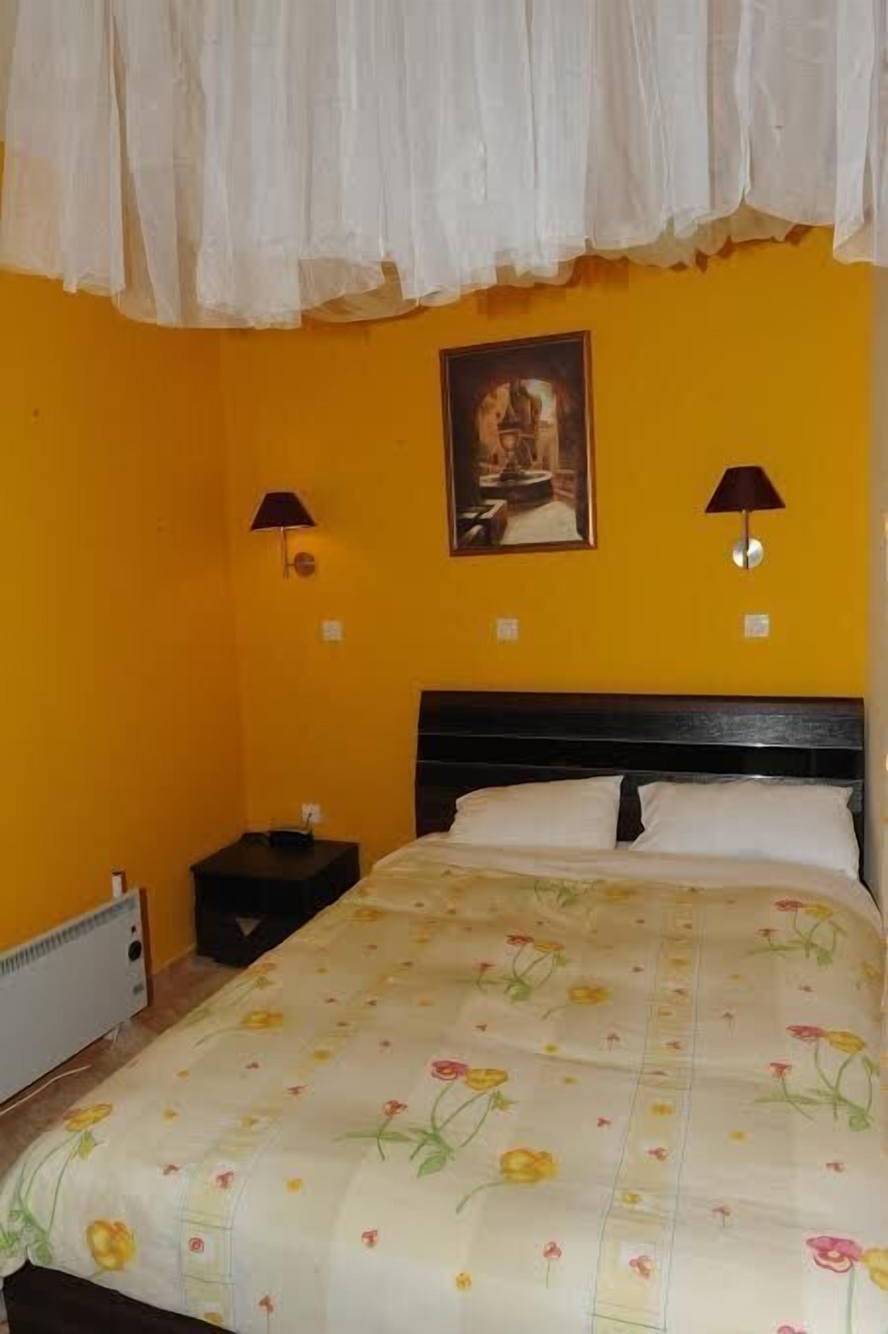 Una habitación con cama, dos lámparas de noche, un cuadro en la pared y un calefactor en el suelo.