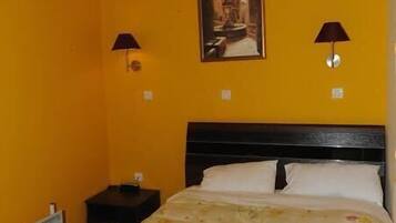 Una habitación con cama, dos lámparas de noche, un cuadro en la pared y un calefactor en el suelo.