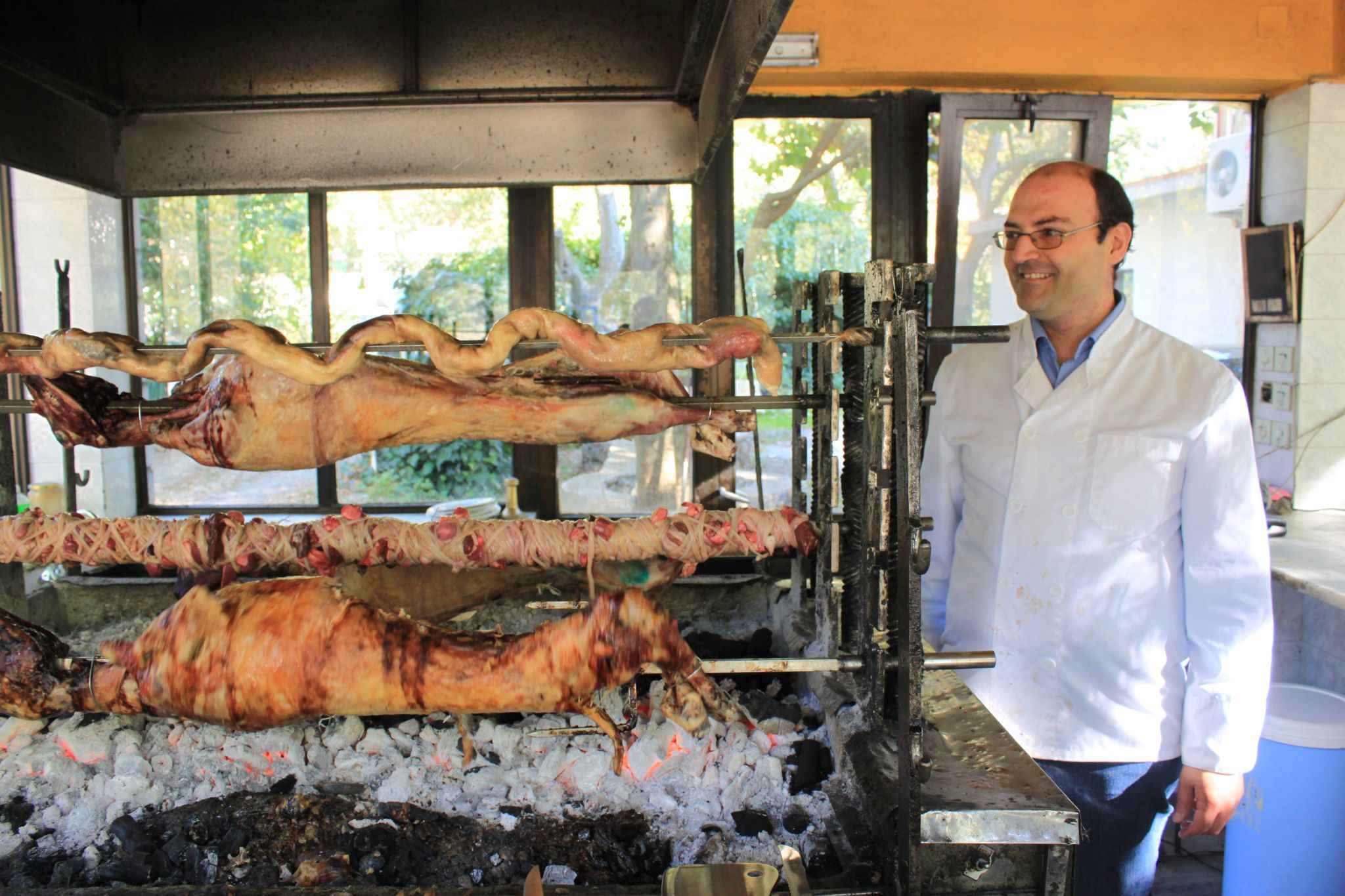 A man in a white lab coat standing next to a large spit-roasted pig on a rotisserie.