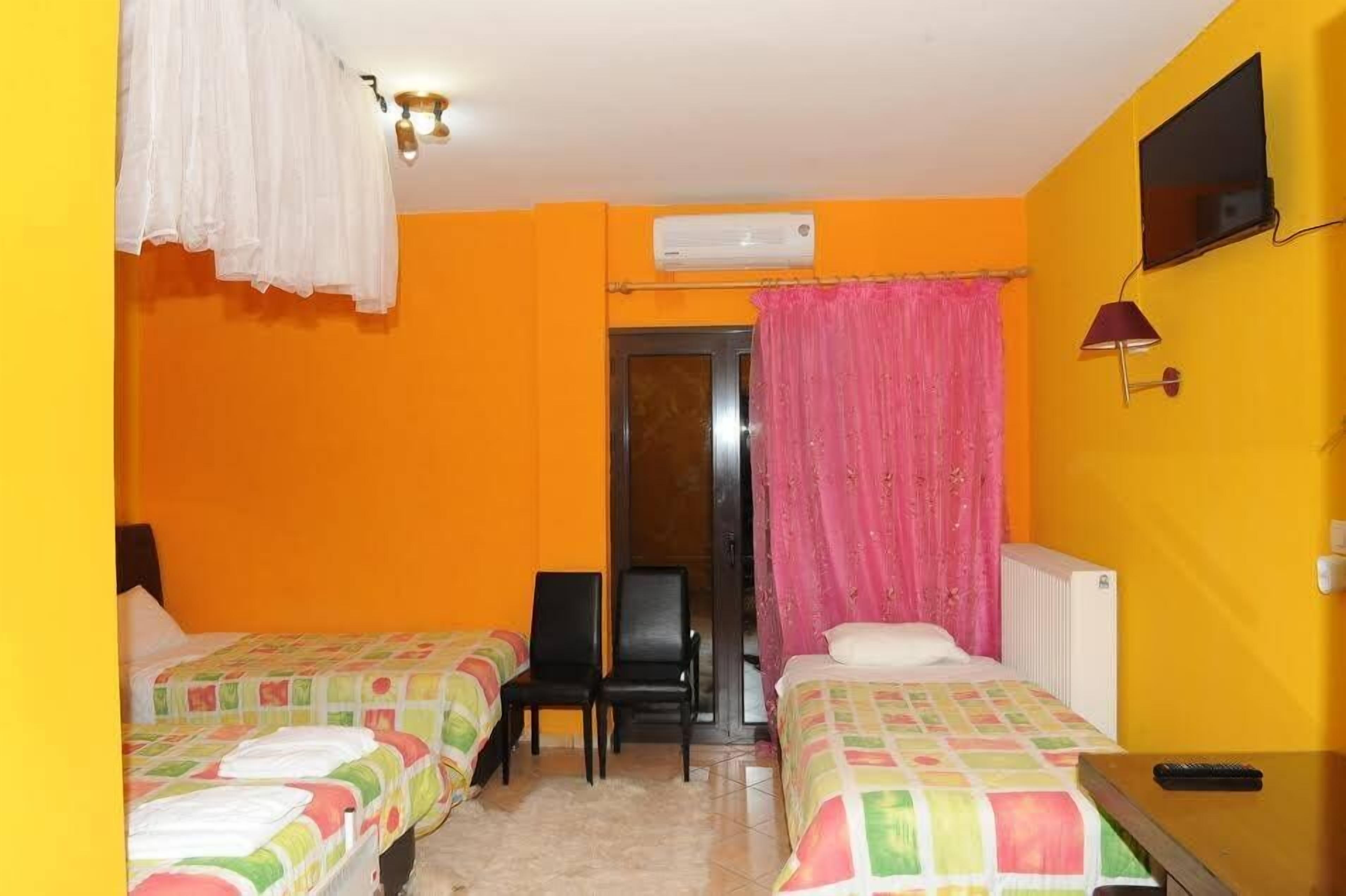 Une chambre d’hôtel avec deux lits, une chaise, un appareil de climatisation, un téléviseur et une fenêtre avec des rideaux.