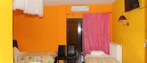 Une chambre d’hôtel avec deux lits, une chaise, un appareil de climatisation, un téléviseur et une fenêtre avec des rideaux.