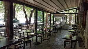 Een terras met tafels en stoelen, grote ramen en uitzicht op de straat.