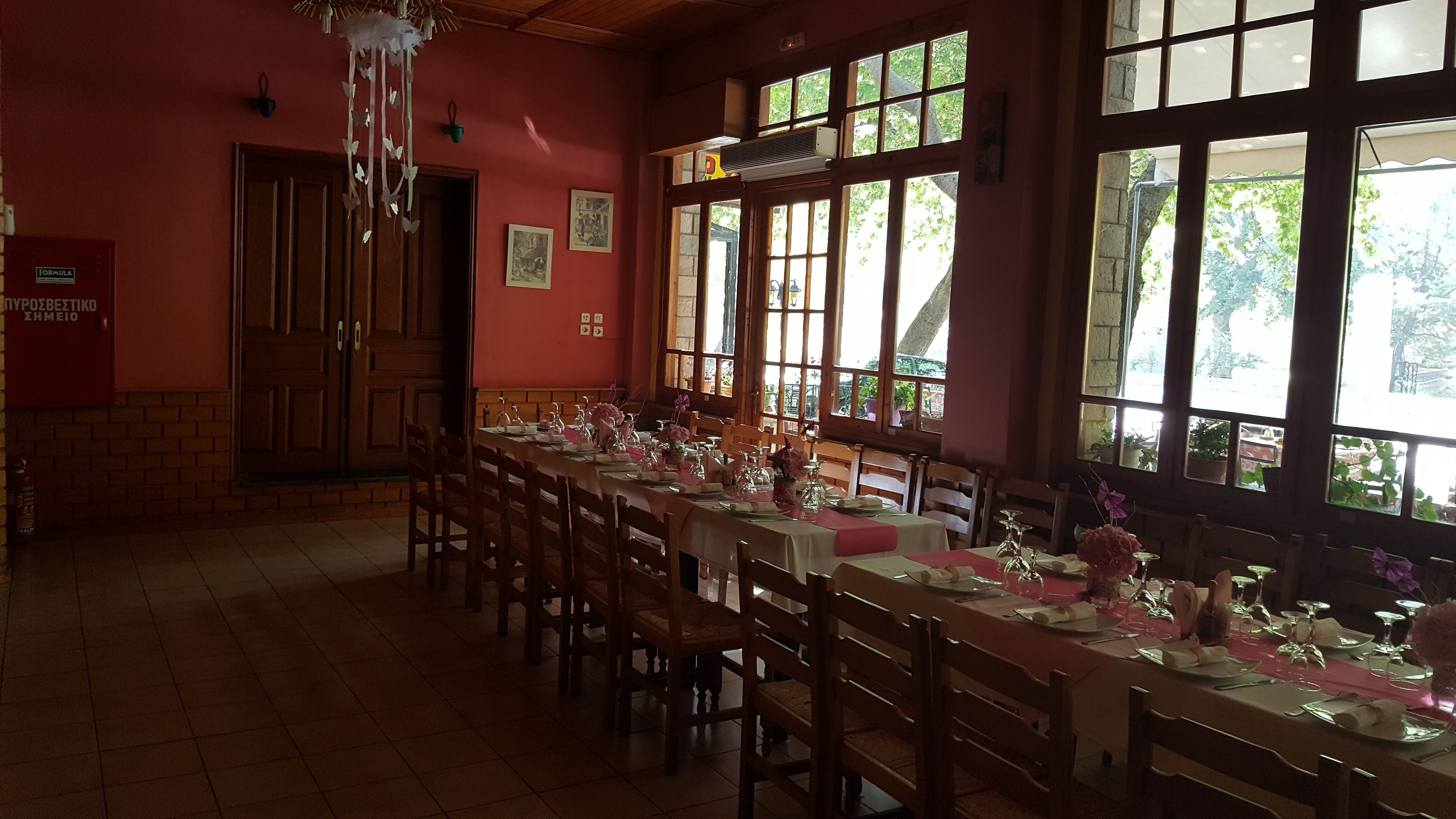 Uma longa mesa de jantar posta com cadeiras, grandes janelas e uma parede vermelha.