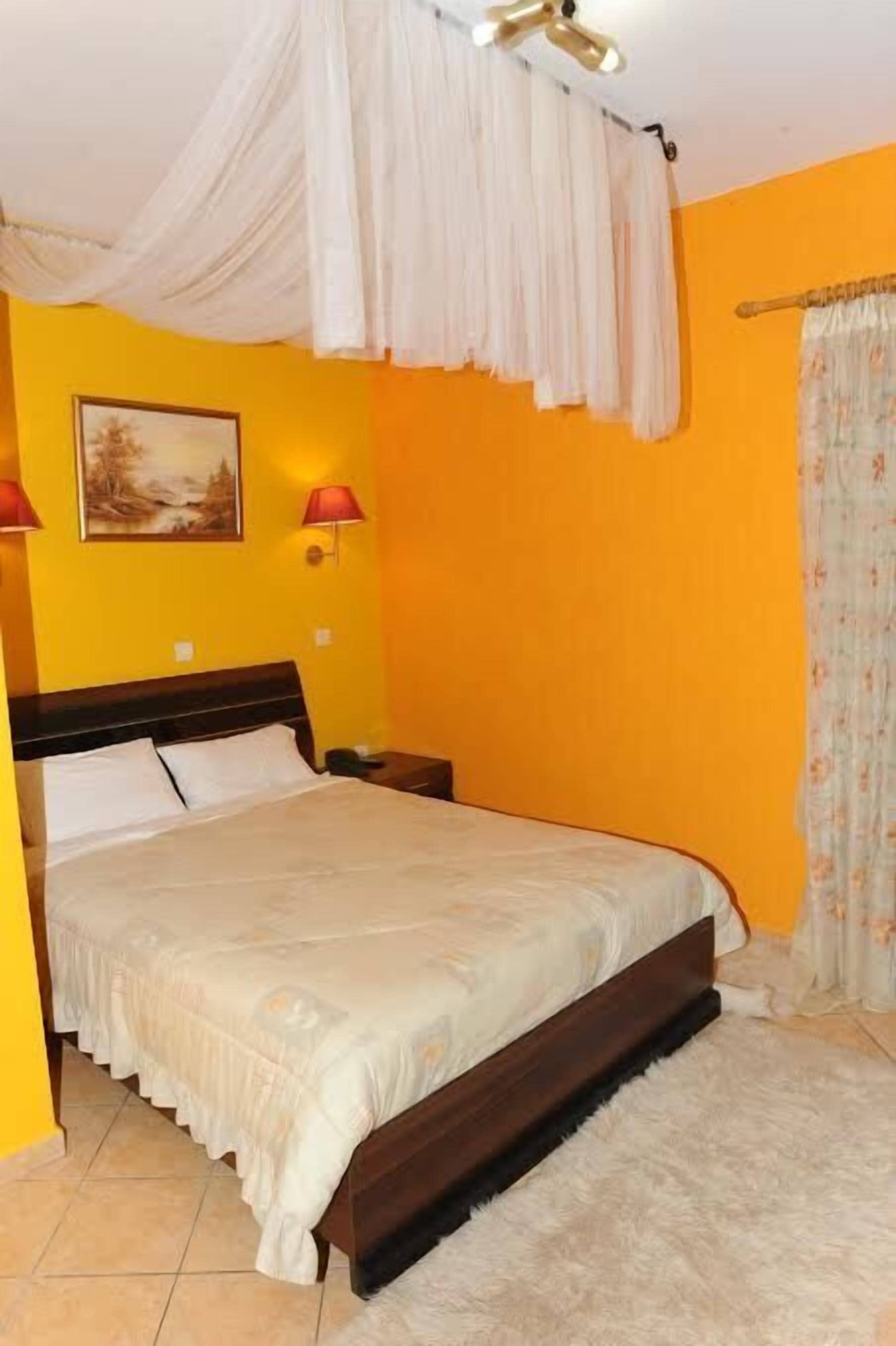 Quarto com cama, mesa de cabeceira, abajur, quadro na parede e cortina.