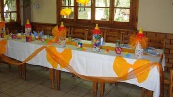 A long dining table with a white tablecloth, decorated with yellow ribbons and various items like bottles and toys.