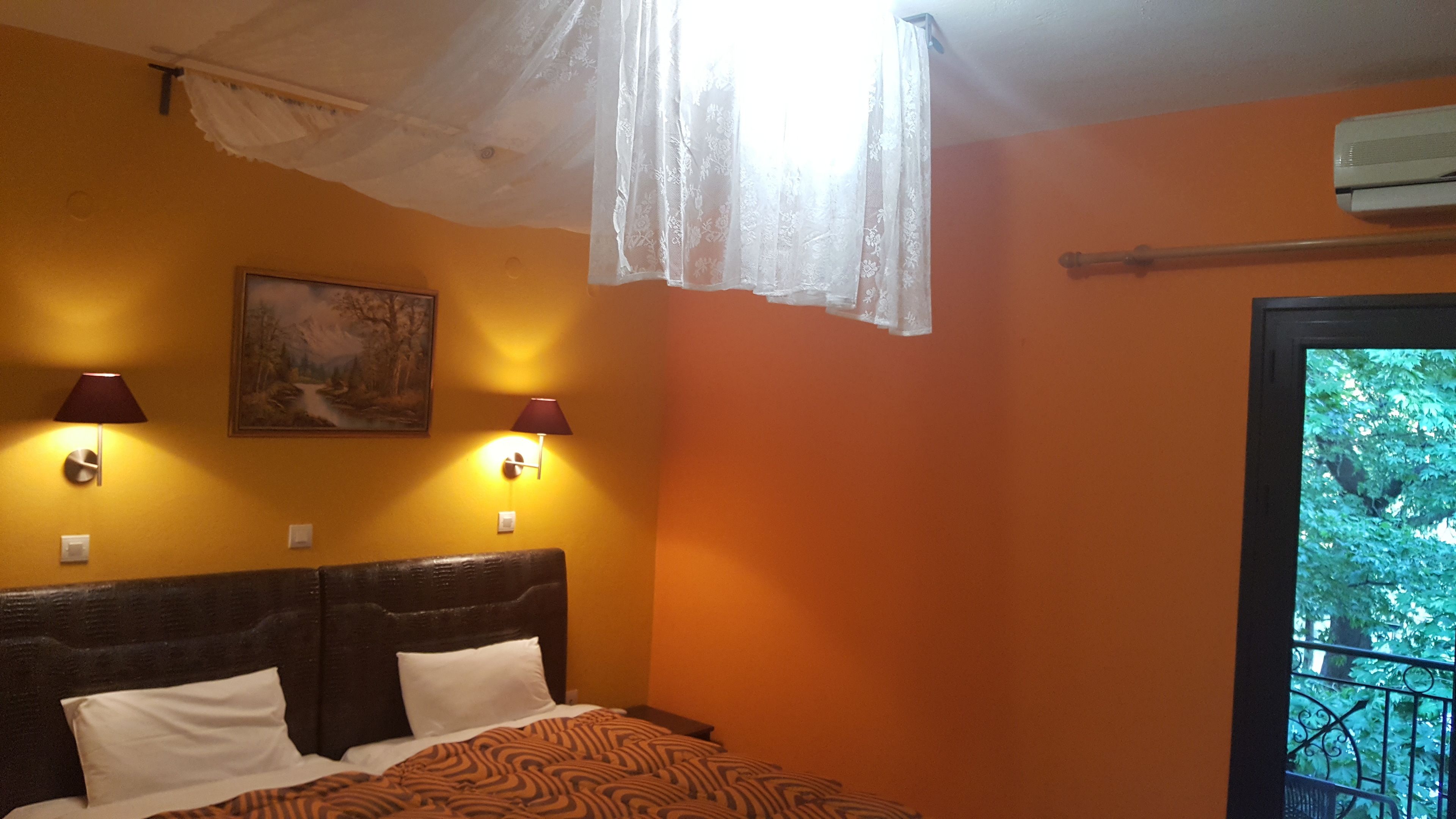 Un dormitorio con cama, dos lámparas de pared, un cuadro y un equipo de aire acondicionado.