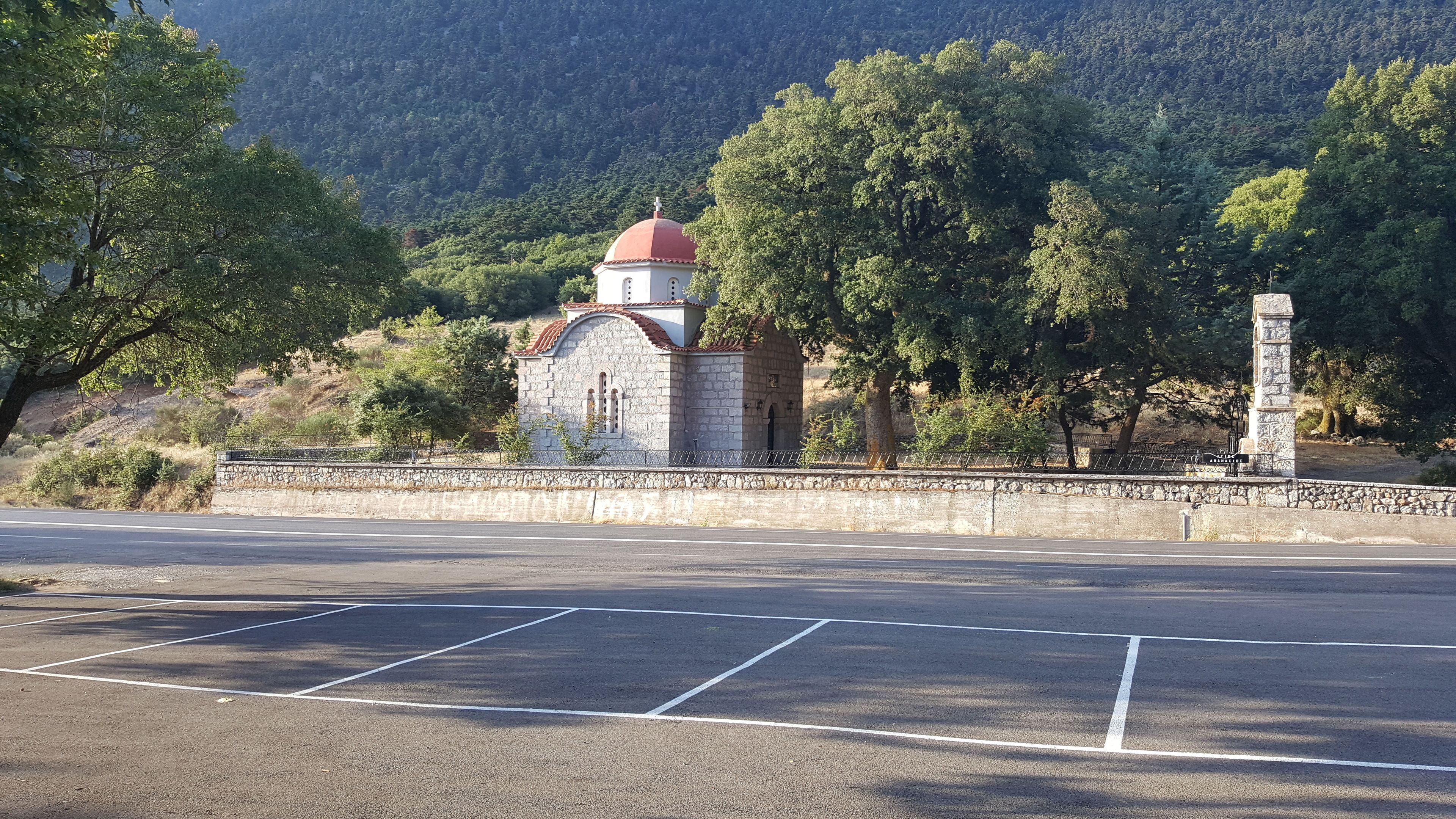A small stone church with a red dome, surrounded by trees and hills.