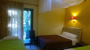 Hotelkamer met twee bedden, een stoel, een nachtkastje, een lamp en uitzicht op groen.