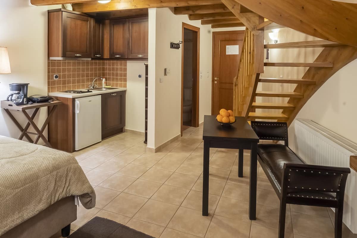 A spacious room with a high ceiling, wooden beams, a kitchen area, a dining table with chairs, and a staircase.