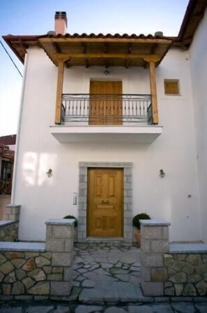 A two-story building with a wooden door, a balcony with a metal railing, and stone steps leading to the entrance. - Odos Oneiron (Distomo-Arachova-Antikyra)