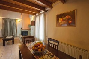 A dining area with a wooden table, chairs, a bowl of fruit, and a painting of fruit on the wall. - Odos Oneiron (Distomo-Arachova-Antikyra)