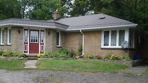 A two-story house with a red door, a satellite dish, and a small front porch. - Inn Towne Cottage (Bancroft)