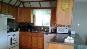A kitchen with wooden cabinets, a stove, a microwave, and a sink. - Inn Towne Cottage (Bancroft)