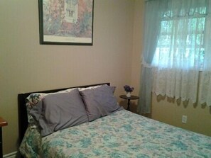 A bedroom with a bed, a small table with a vase, and a window with curtains.