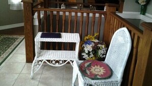 A white wicker chair with a floral cushion, a small table with a blue cloth, and a wooden railing. - Inn Towne Cottage (Bancroft)