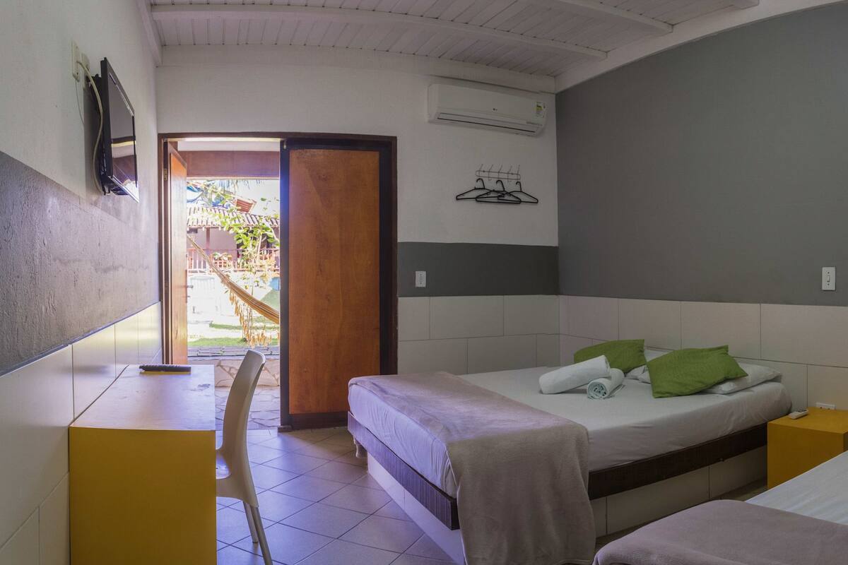 Una habitación con dos camas, un escritorio y una silla. Hay una puerta que da a un espacio al aire libre con una hamaca y una terraza de madera.