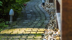 A cobblestone pathway flanked by greenery and a building with a tiled roof. - Pousada Tubes - Hostel (São Sebastião)