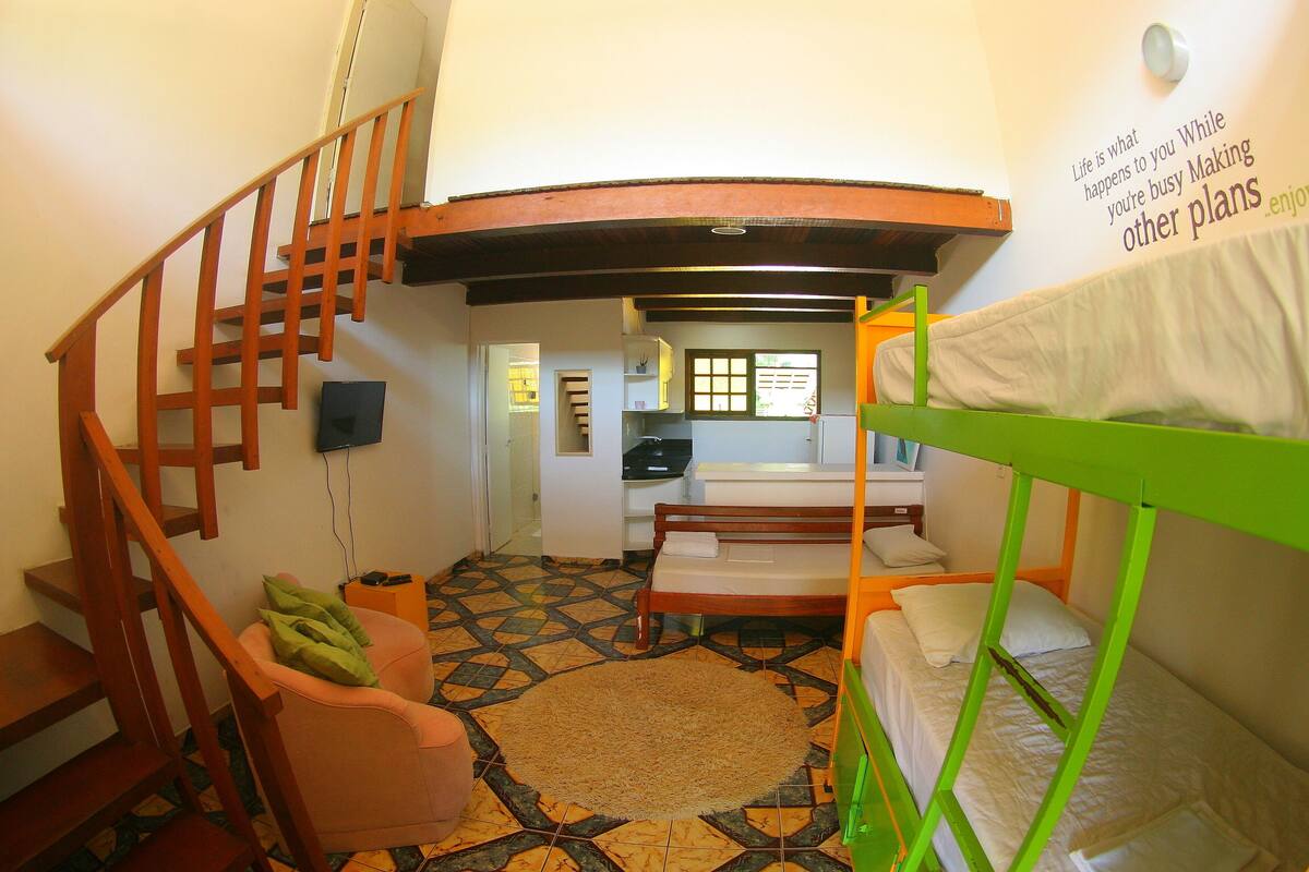 Una habitación pequeña con una litera, una silla, una mesita y una escalera.
