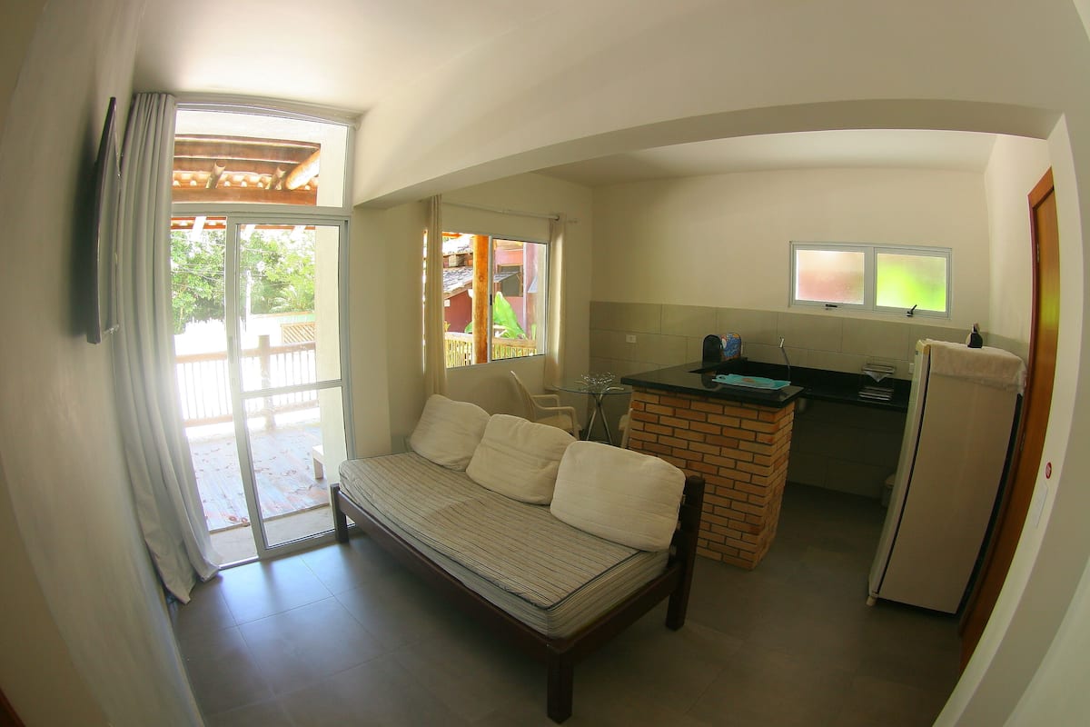 Un espacio habitable compacto con cama, kitchenette y puerta corrediza de vidrio que da a un área exterior.