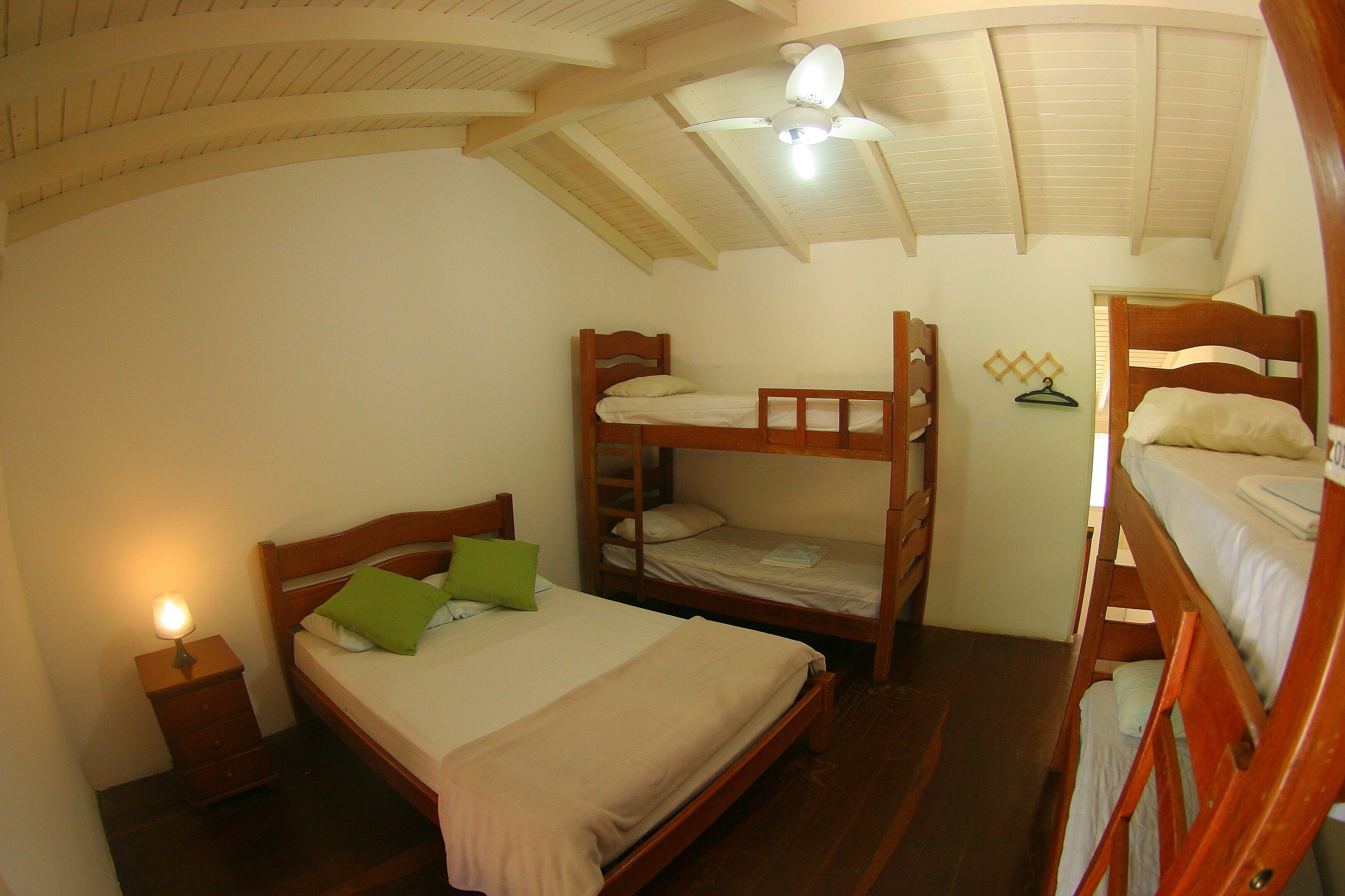 Un dormitorio con literas, una cama individual, una mesita de noche con lámpara y un ventilador de techo.