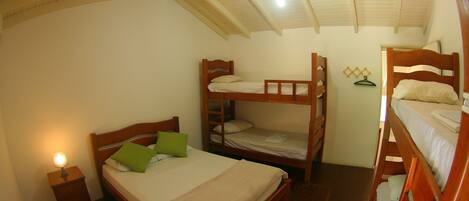 A dormitory room with bunk beds, a single bed, a nightstand with a lamp, and a ceiling fan.