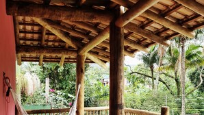 A wooden deck with a hammock, wooden railings, and a view of lush greenery. - Pousada Tubes - Hostel (São Sebastião)