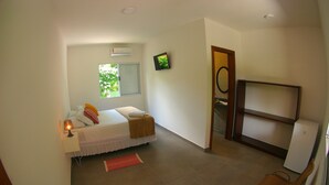 A bedroom with a bed, bedside lamp, window, air conditioner, and a small table. - Pousada Tubes - Hostel (São Sebastião)