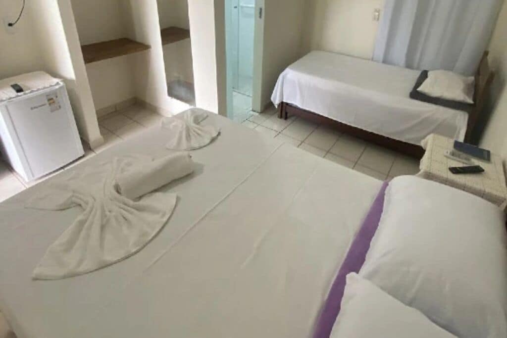 Quarto de hotel com duas camas, um minibar e uma casa de banho com porta de vidro.