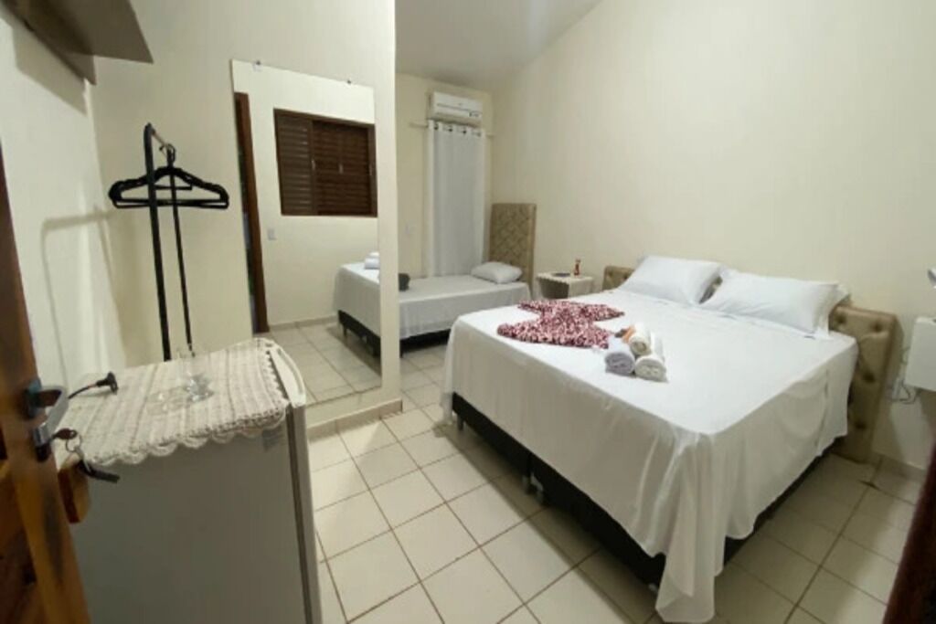 Quarto de hotel com cama, mesa de cabeceira, cabideiro e área de chuveiro.