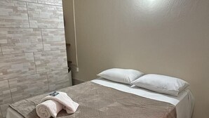 Ein Einzelbett mit einer beigen und braunen Bettdecke, weißen Kissen und einem zusammengerollten Handtuch daneben.