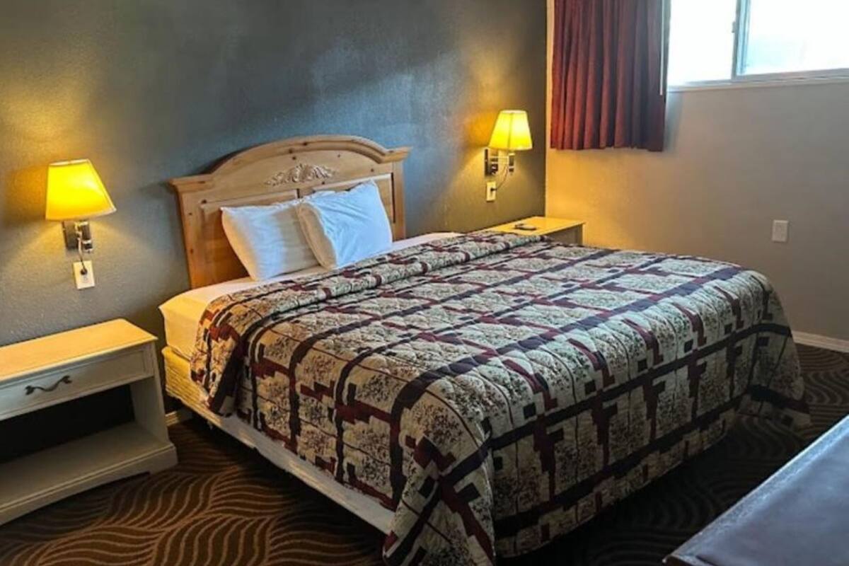 A hotel room with a large bed, two bedside lamps, a nightstand, and a window with curtains.