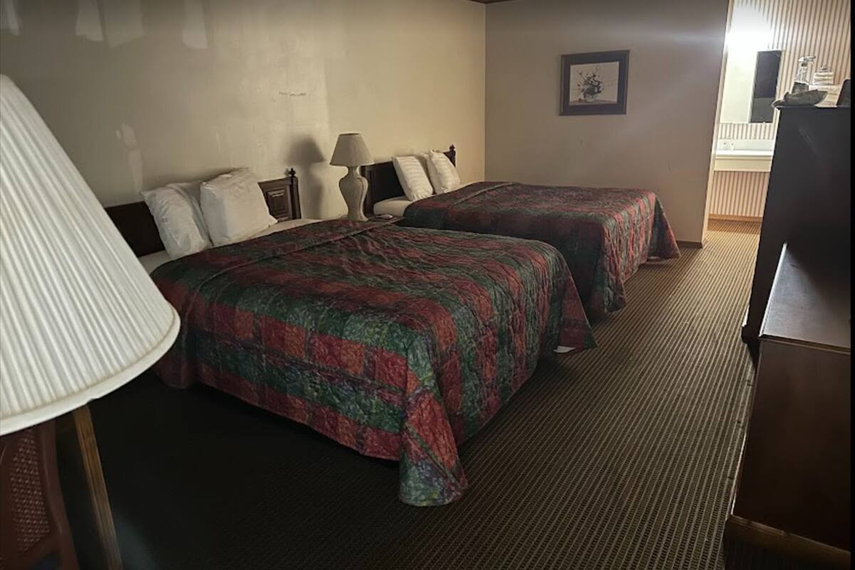 A hotel room with two beds, a lamp, a framed picture on the wall, and a television.