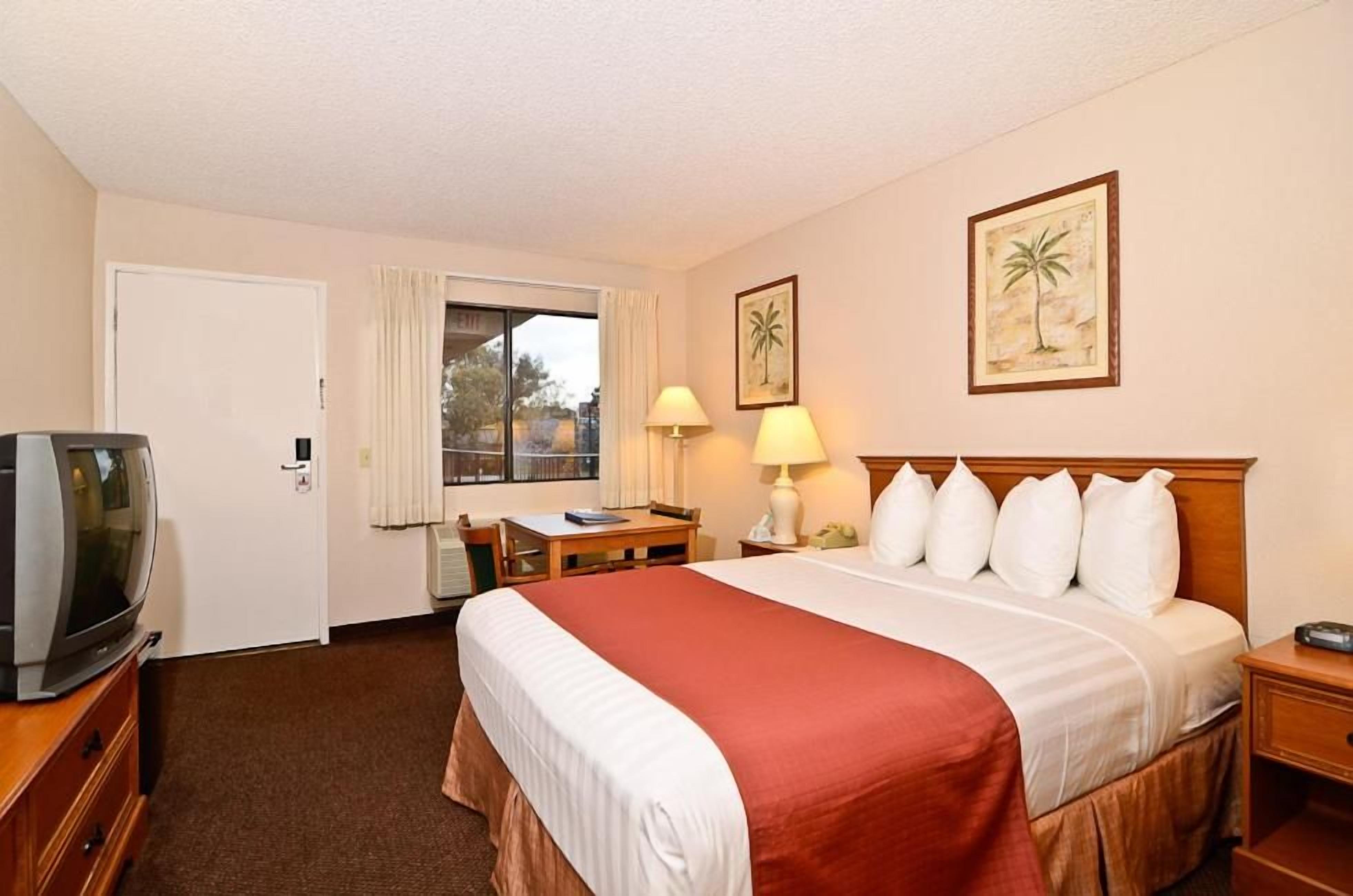 Ein Hotelzimmer mit einem Bett, einem Schreibtisch, einem Fernseher und zwei gerahmten Bildern an der Wand.