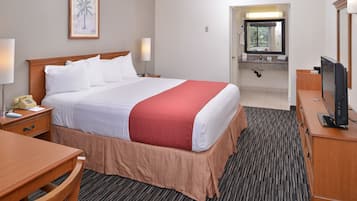 Une chambre d’hôtel avec un grand lit, un bureau, une chaise, une télévision et une salle de bain visible à travers une porte ouverte.