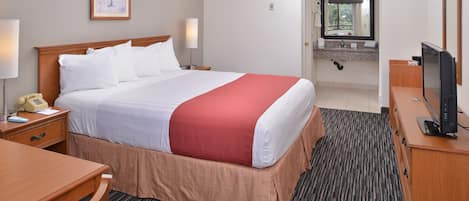 A hotel room with a large bed, a desk, a chair, a television, and a bathroom visible through an open door.
