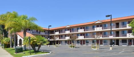 A multi-story hotel with a red-tiled roof, balconies, and a parking lot.