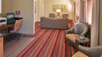 Ein Hotelzimmer mit Streifenmuster-Teppich, einem Schreibtisch mit Computer, einem Sessel und einer Couch.