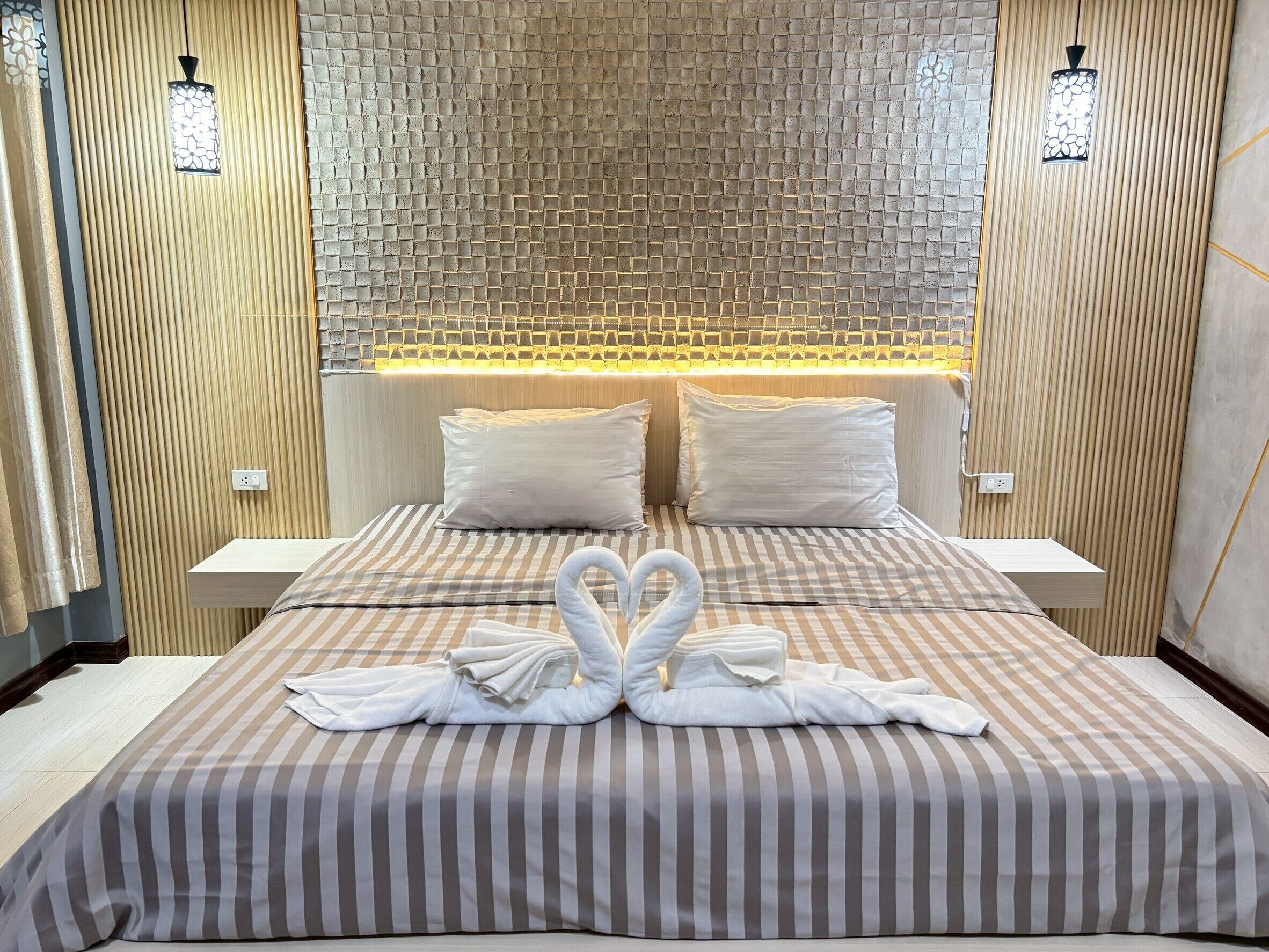 Habitación de hotel con una cama, dos almohadas, cabecera con diseño texturizado y dos lámparas fijadas a la pared.