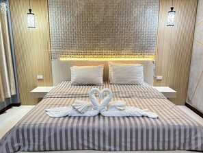 A hotel room with a bed, two pillows, a headboard with a textured pattern, and two wall-mounted lamps.