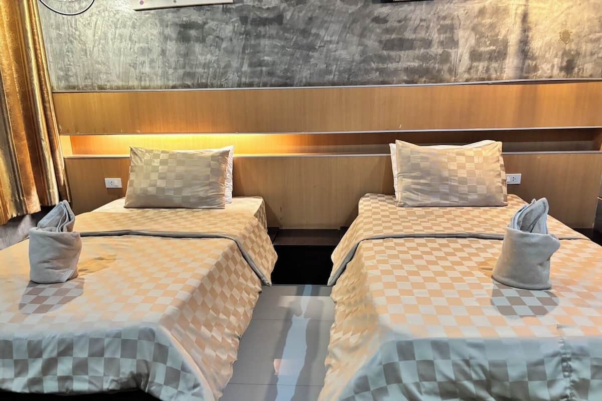 A hotel room with two beds, each with a checkered bedspread and pillows. There is a wooden headboard and a wall with a textured pattern.