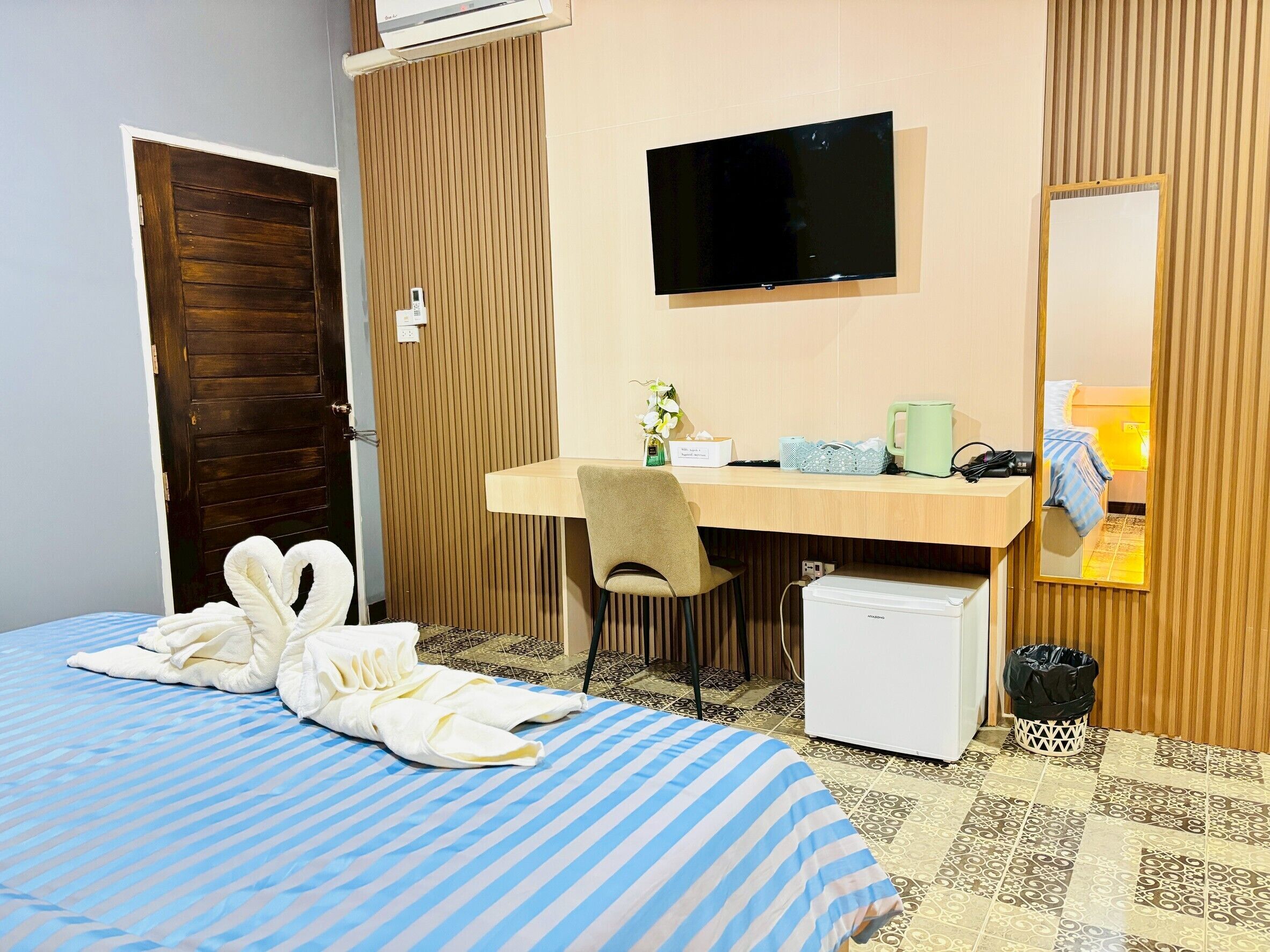 Habitación de hotel con cama, escritorio con silla, televisión, refrigerador pequeño y cesto de basura.