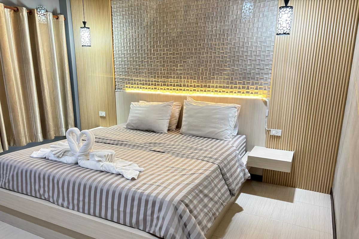 A hotel room with a bed, a nightstand, a wall-mounted lamp, and a decorative wall panel.
