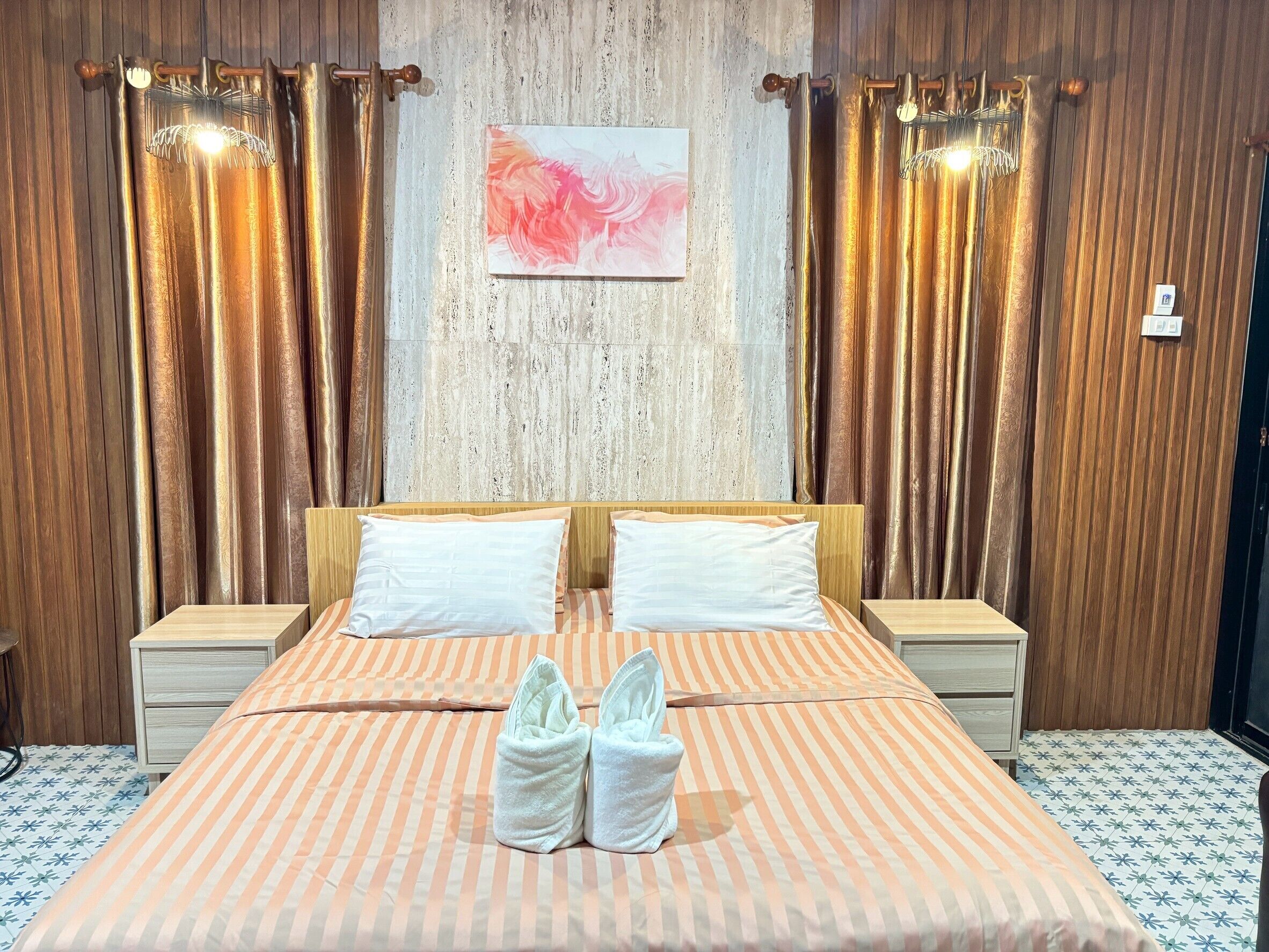 A hotel room with a bed, two pillows, a headboard, and a painting on the wall.