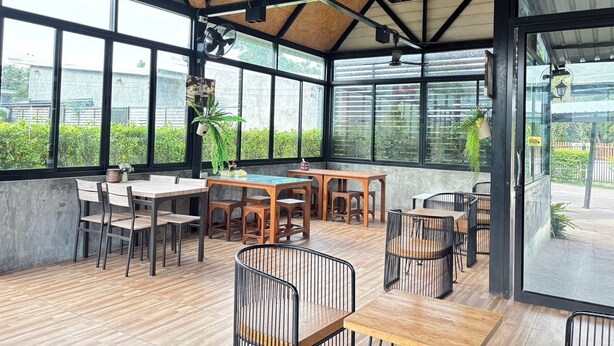 A spacious indoor area with wooden flooring, multiple tables and chairs, and large windows offering views of greenery outside. - Le Park 23 Boutique Resort (Roi Et)