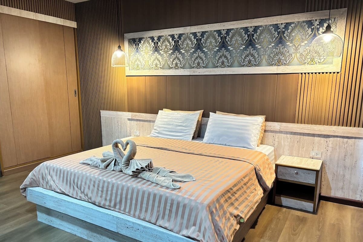 A neatly made bed with a striped bedspread and two pillows, a bedside table with a lamp, and a decorative wall panel above the bed.